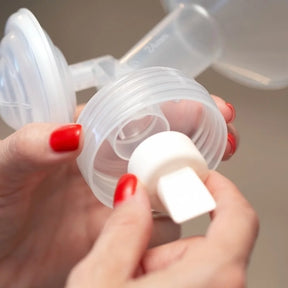 Close-up of hands assembling a breast pump valve with clear plastic parts