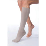 Beige knee-high compression sock on lower leg, medical support hosiery for circulation