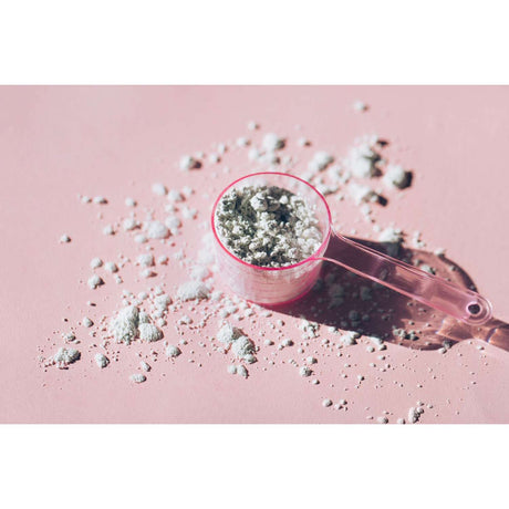 Plastic scoop with medical powder supplement on pink background