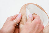 Hands removing adhesive backing from a beige ostomy bag for medical use