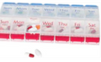 Weekly pill organizer with compartments labeled for each day, holding assorted pills