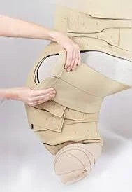 Person applying beige medical compression garment on leg and foot for lymphedema care