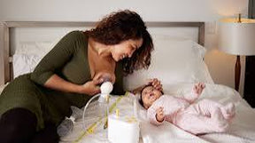 Mother using breast pump beside infant on bed, home medical supplies visible