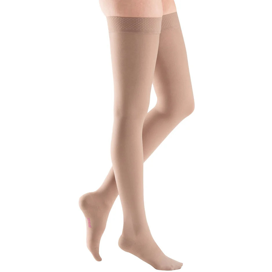 Beige medical compression thigh-high stockings on legs against white background