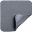 Square grey foam wound dressing pad with one corner peeled back, medical supply.
