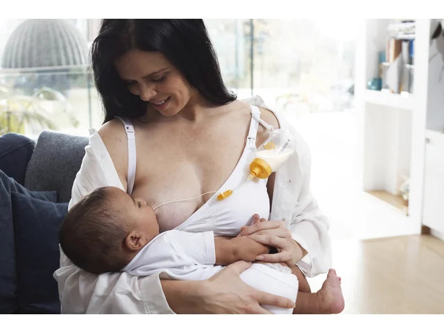 Mother using supplemental nursing system to breastfeed infant at home, medical supply aid