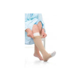 Person in robe putting on beige medical compression stocking, sitting on chair