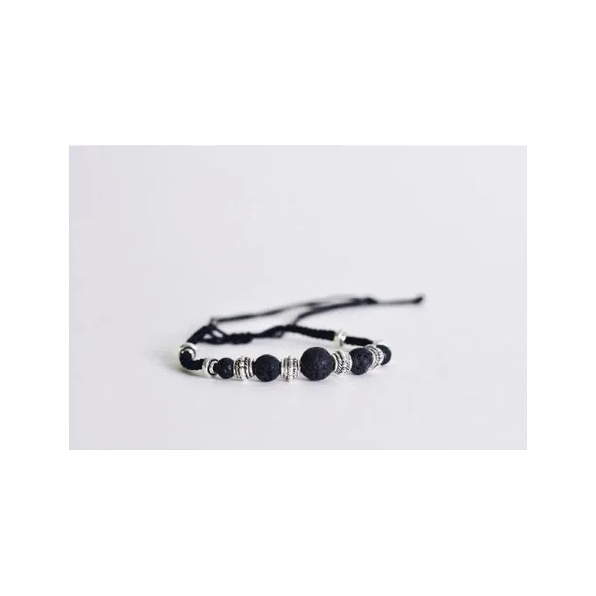 Adjustable black lava bead bracelet with silver accents on white background