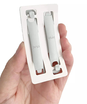 Hand holding two Elvie gray medical device clips in white packaging