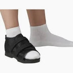 Person wearing medical post-op shoe on left foot, right foot in white sock, on white background