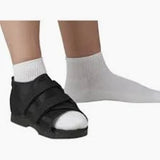 Person wearing medical post-op shoe on left foot, right foot in white sock, on white background