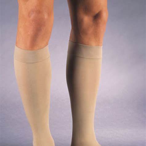 Man wearing beige medical compression socks for leg support against gray background.