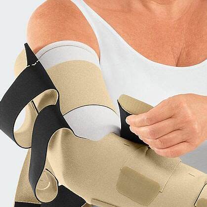 Person wearing beige medical arm brace, securing adjustable straps for compression support