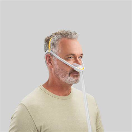 Man wearing nasal CPAP mask for sleep apnea therapy against plain background